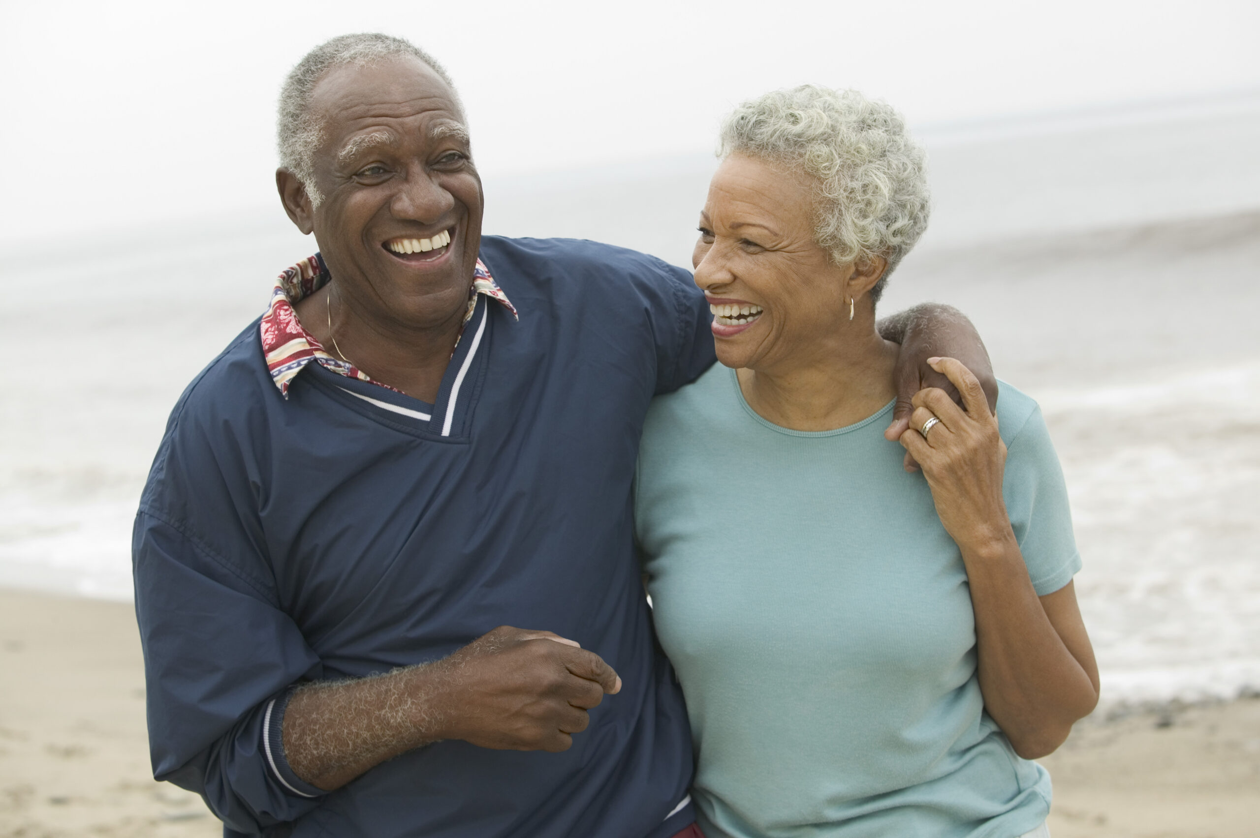An older couple laughing together while walking on the beach